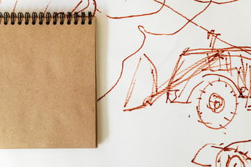  image: a spiral notebook with square sheets of crafting paper on the background of a picture with tractors and abstractions, which is drawn with markers. Place for text