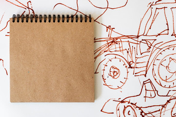  image: a spiral notebook with square sheets of crafting paper on the background of a picture with tractors and abstractions, which is drawn with markers. Place for text