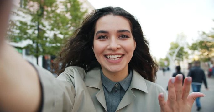 POV slowmotion of attractive woman making online video call in the street talking gesturing looking at camera outdoors. Communication and youth concept.