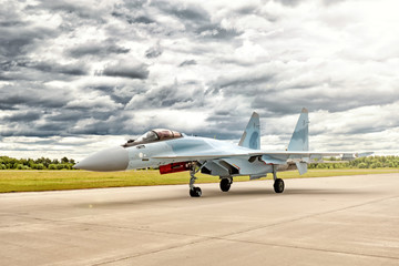 Fototapeta na wymiar modern military fighter jet airplane in blue and grey camouflage color taxiing to airport runway for take off against dramatic clouds sky landscape background