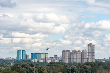 View of the new residential area of Moscow among the green grove on the background of clouds in the blue sky.