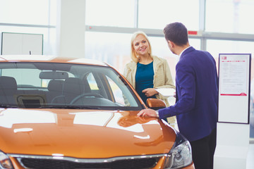 Dealer with woman stands near a new car in the showroom.