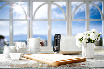 White wooden desk in kitchen and blurred background of window and summer landscape of sun and sea 