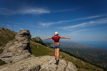 Fototapeta premium The concept of overcoming, rest and freedom. A woman with tanned legs is standing on top with her arms wide open on either side. Near the rocks of unusual shape. 