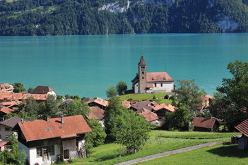 Fototapeta na wymiar Old church and timber chalets in Brienz, Switzerland. Turquoise water of Lake Brienz.
