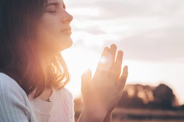 Foto op Plexiglas Teenager Girl closed her eyes, praying in a field during beautiful sunset. Hands folded in prayer concept for faith, spirituality and religion. Peace, hope, dreams concept © Анастасія Стягайло