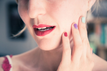 Fototapeta premium Attractive red lip stick: Blonde young woman with colorful nail polish is looking herself in the mirror. Cut out of the face.