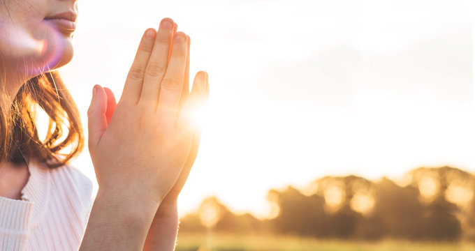 Teenager Girl closed her eyes, praying in a field during beautiful sunset. Hands folded in prayer concept for faith, spirituality and religion. Peace, hope, dreams concept