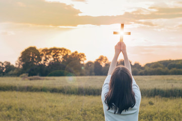 Teenager Girl holding a the cross in hand during beautiful sunset. Hands folded in prayer concept...