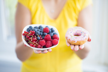 Woman holding bowl with healthy berries and colourful donut, choose healthy eating  