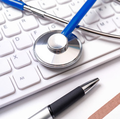 Stethoscope on computer keyboard on white background. Physician write medical case long term care treatment concept, close up, macro, copy space