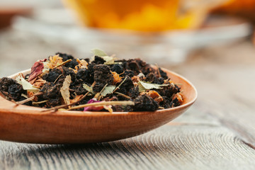 Fototapeta na wymiar Black tea with herbs in wooden spoons on a wooden board