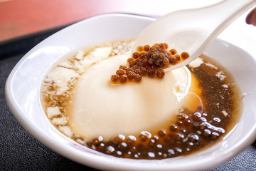 Popular Taiwan gourmet - Dessert of tapioca pearl ball (bubble) mixed bean curd tofu pudding (douhua, dou hua) in white bowl, close up, lifestyle