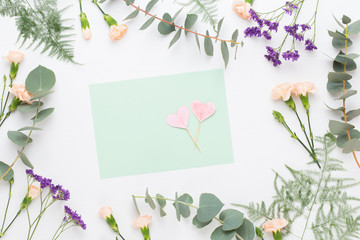Flowers composition. Paper blank, carnation flowers, eucalyptus branches on pastel  background. Flat lay, top view, copy spaceFlat lay stiil life.
