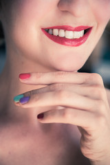 Fototapeta premium Attractive red lip stick: Blonde young woman with colorful nail polish is looking herself in the mirror. Cut out of the face.