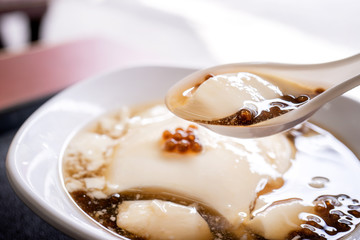 Popular Taiwan gourmet - Dessert of tapioca pearl ball (bubble) mixed bean curd tofu pudding (douhua, dou hua) in white bowl, close up, lifestyle