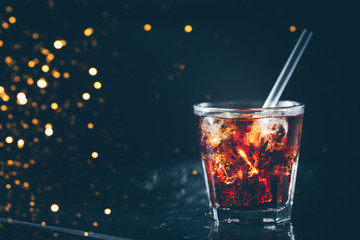 Cuba libre cocktail at the bar stand. Dark background. Horizontal. Festive holiday bokeh