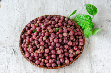 Juicy ripe red berries of a gooseberry in a small wicker round basket and a sprig of fresh basil on a wooden background
