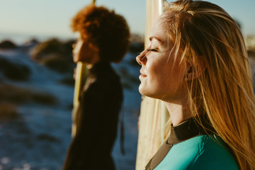 Profiles of two female surfers on beach in sunlight