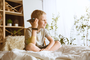 Fototapeta premium Boy using different gadgets at home. Little model with smart watches, smartphone or tablet and headphones. Making selfie, chating, gaming, watching videos. Interaction of kids and modern technologies.
