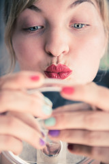 Attractive red lip stick: Blonde young woman with colorful nail polish is looking herself in the mirror. Kiss mouth.