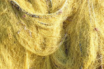 Yellow fishing net closeup pile at a Greek harbor on a jetty at summer season