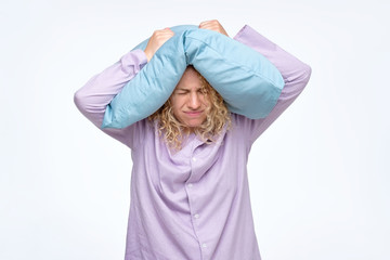 Young curly woman covering head with pillow trying to sleep. Loud noise or insomnia concept.