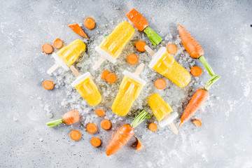Vegetable gelato. Vegan carrot ice cream popsicles with organic baby carrots, old rustic wooden background.