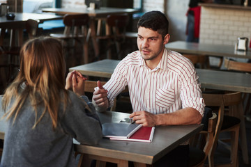 People have conversation in the restaurant. Man in shirt with stripes speaks to a girl
