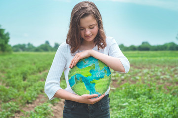 Teen girl holding planet in hands against green spring background. Earth day holiday concept....