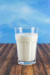 A glass of milk on a wooden table, copy space and blue sky background