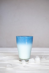 Trendy seasonal milk drink with a teaspoon of blue. Refreshing summer cocktail of white and blue color with ice cubes falling into a glass and spray
