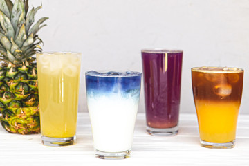assortment of fresh iced fruit drinks on a white background with chopped slices of pineapple and orange, closeup