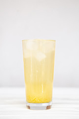 A refreshing summer cocktail of yellow color in a high transparent glass with pineapple slices on a white background.