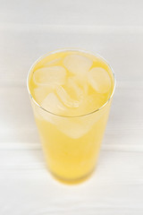 A refreshing summer cocktail of yellow color in a high transparent glass with pineapple slices on a white background.