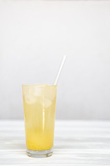 A refreshing summer cocktail of yellow color in a high transparent glass with pineapple slices on a white background.