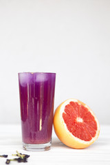 a high glass filled with a cold summer drink of purple in the background of a threaded grapefruit