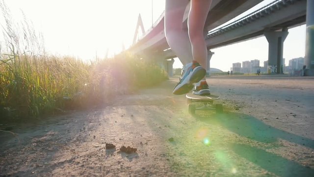 Young woman with nice legs riding skateboard under the urban bridge - bright sunlight