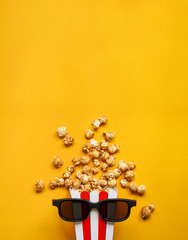 Popcorn in a red and white cardboard box with glasses for a 3D movie on the yellow back. Popcorn in red striped bucket on yellow background. Flat lay concept. - obrazy, fototapety, plakaty