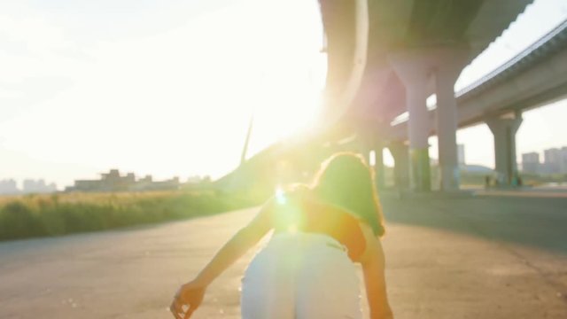 Young woman turning to the camera, smile and go ride a skateboard - beautiful sunset