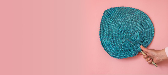 Woman hand holding a blue fan on pink background with copy spac