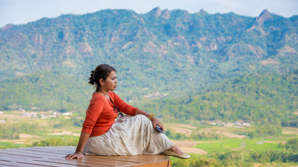 Young Asian woman sitting and looking out of the scenic countryside of central java, Indonesia.