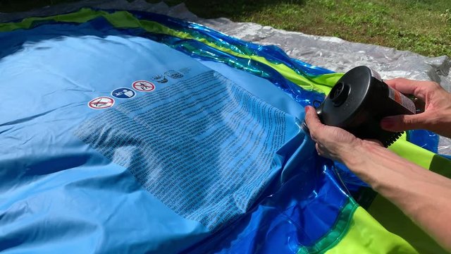 [Static, point of view] Person is pumping up plastic pool with small electric pump. Battery pump filling inflatable pool with air.