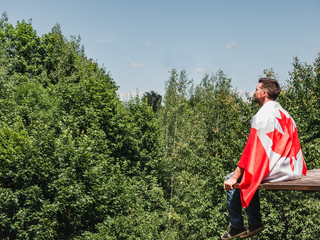 Naklejka premium Attractive man in jeans and denim shirt waving a Canadian Flag against a clear, sunny, blue sky. View from the back, close-up. National holiday concept