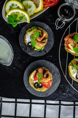 small canape with pink salmon fish, cucumber, tomato, olive and lemon on a black background. dark food photo