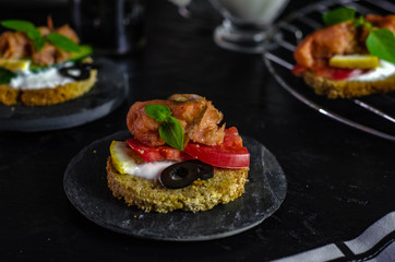 small canape with pink salmon fish, cucumber, tomato, olive and lemon on a black background. dark food photo