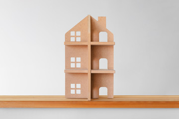 Toy wooden house on a wooden shelf on a gray background. Symbol of real estate.