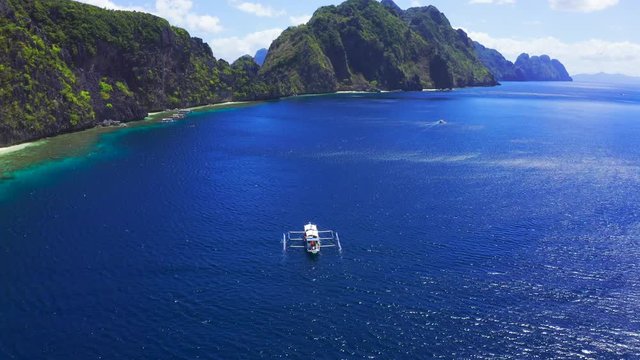 Aerial drone view of white traditional Filipino boat floating on top of clear blue water surface. El Nido, Palawan, Philippines