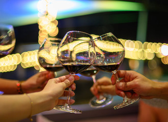 Cropped shot of hand women clinking glasses with red wine in front of bokeh background