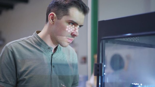 Concentrated quality control expert standing by 3d printing machine in lab, examining printing proccess and making notes, closeup tracking left shot